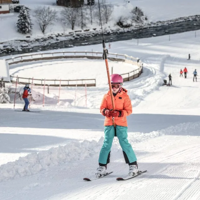 Skifahrende Person in orangefarbener Jacke im Schnee