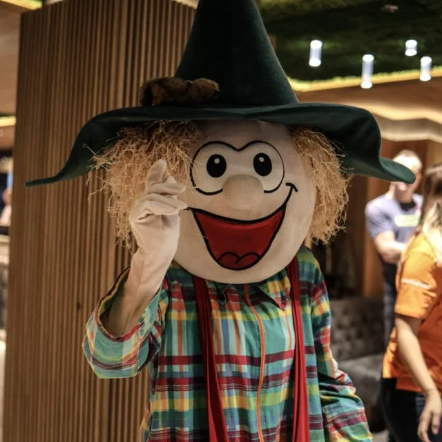 Ein lustiger Maskottchen mit Hut lächelt.