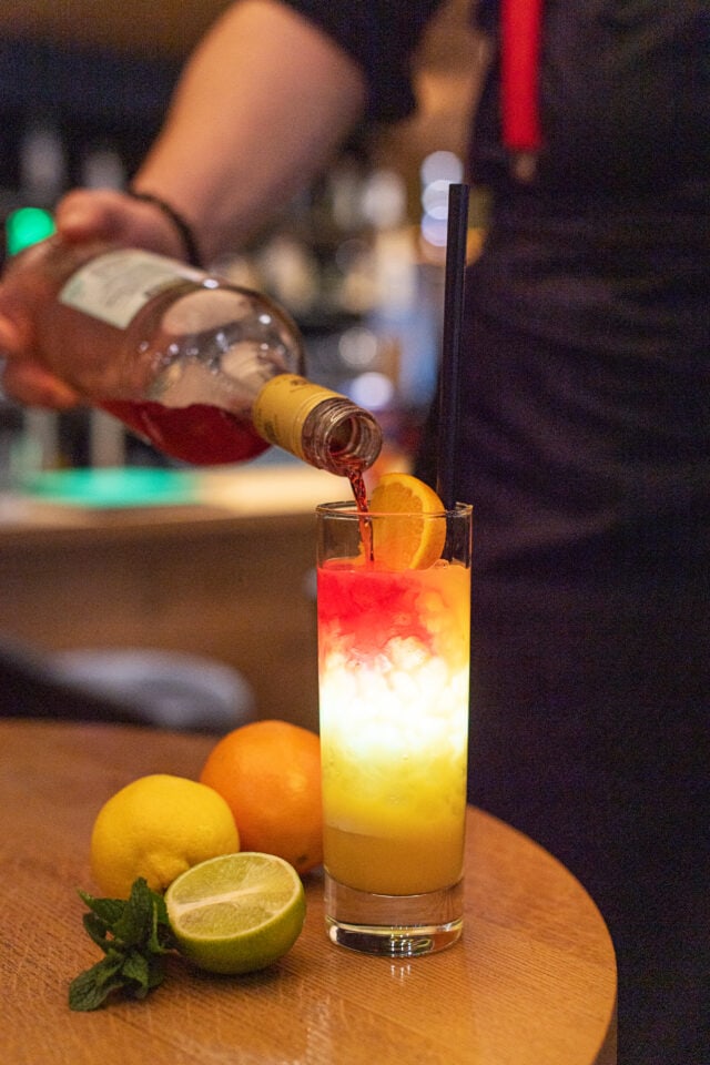 Barkeeper mixt farbenfrohen Cocktail mit Obst.