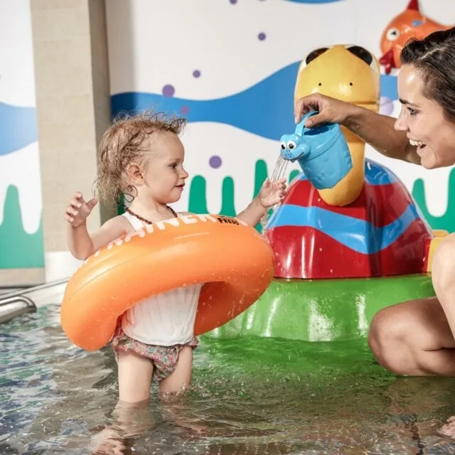 Kind im Wasser mit orangefarbenem Schwimmring.