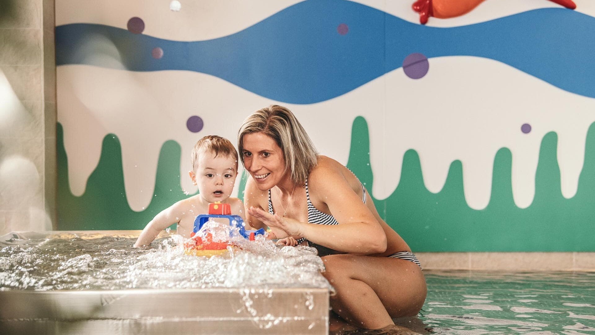 Mutter spielt mit Kind im Wasser.