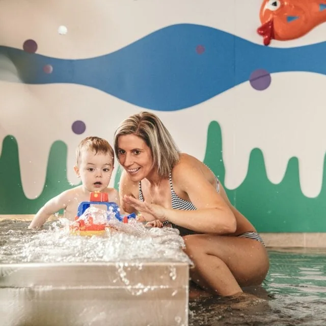 Mutter spielt mit Kind im Wasser.