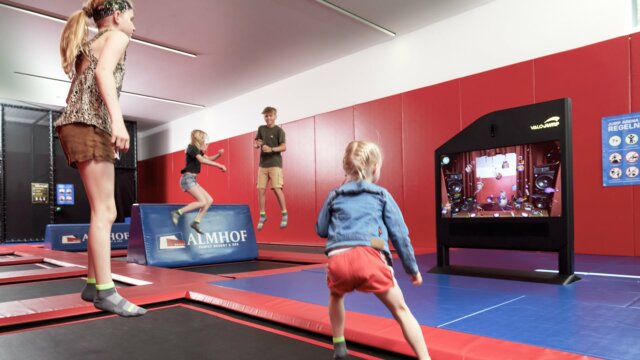 Kinder springen auf Trampolinen in einer Halle.