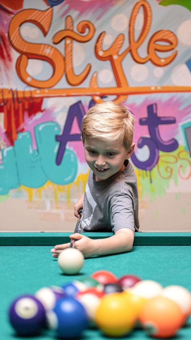 Junge spielt Billard in einem bunten Raum.