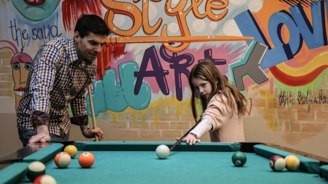 Vater und Tochter spielen Billard zusammen.