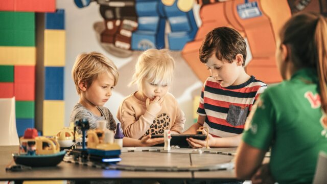 Kinder spielen mit Spielzeug und schauen auf ein Handy.