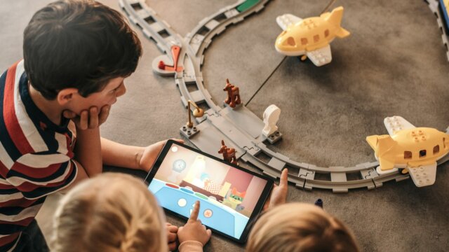 Kinder spielen mit Tablet und Spielzeugautos.