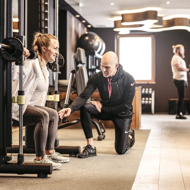 Frau trainiert mit Trainer im Fitnessstudio.