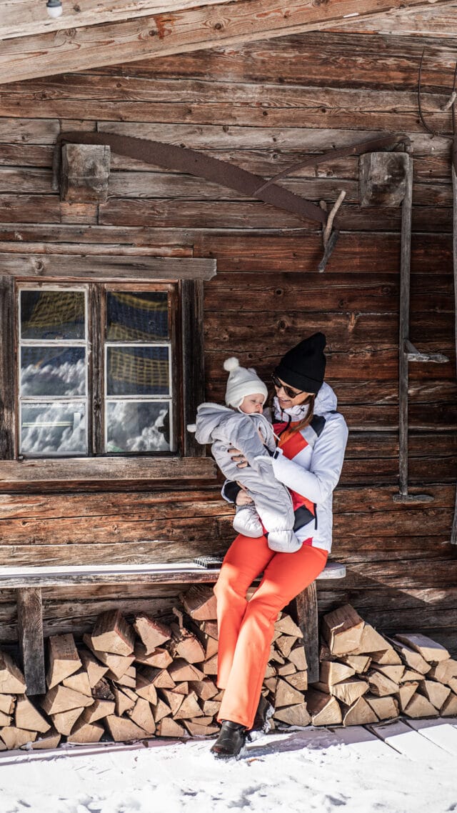 Mutter hält Baby vor einer Holzhütte