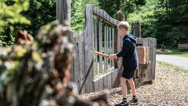 Junge spielt an einem Holzspielgerät im Freien.