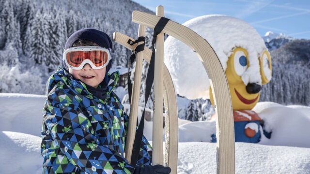 Junge mit Schlitten im Schnee vor Figurbild