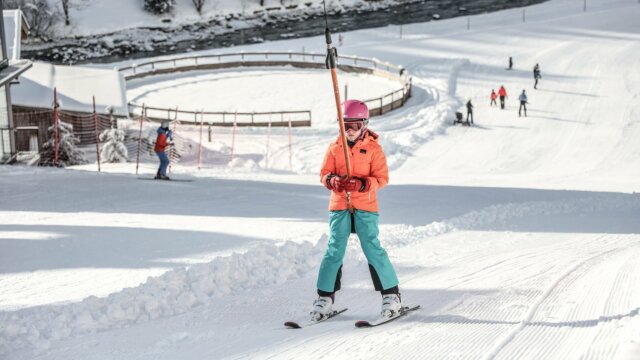 Kind fährt Ski auf einer sonnigen Piste.