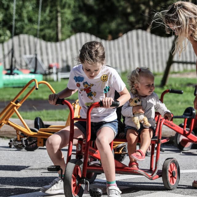 Kinder fahren mit Dreirädern auf dem Spielplatz.