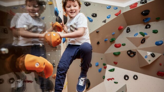 Junge klettert an der Kletterwand mit Freude.
