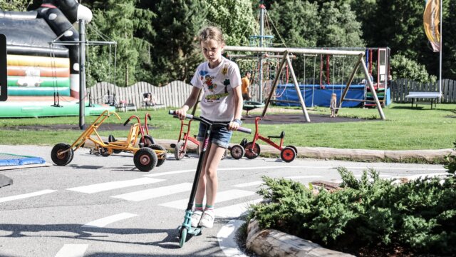 Mädchen fährt mit dem Tretroller im Spielplatz.