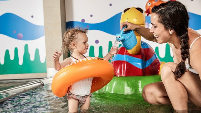 Kind spielt im Wasser mit Mutter und Spielzeug