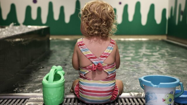 Kleines Kind sitzt am Wasser mit Spielzeug.