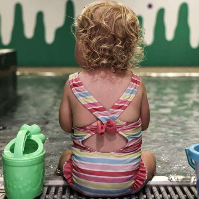 Kleines Kind sitzt am Wasser mit Spielzeug.