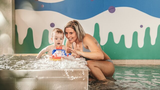 Mama und Kleinkind spielen im Wasser.