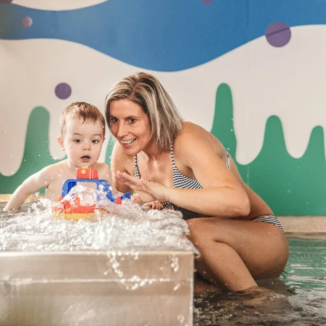 Mama und Kleinkind spielen im Wasser.