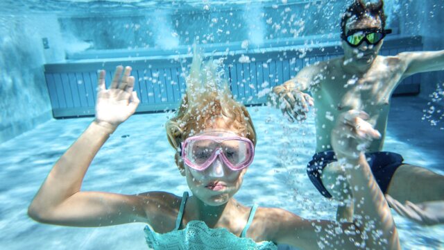 Kind mit Schwimmbrille taucht im Wasser
