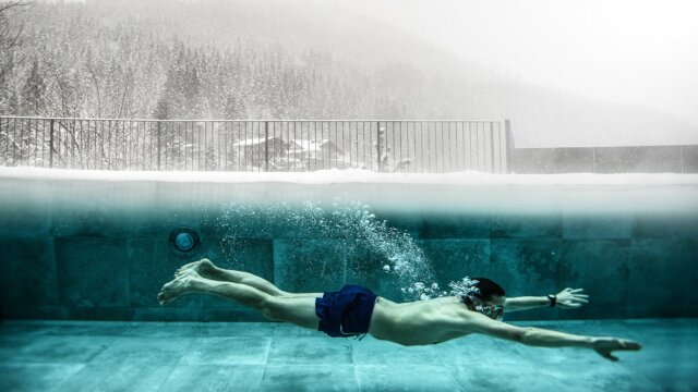 Mann schwimmt im Pool während Schnee fällt.