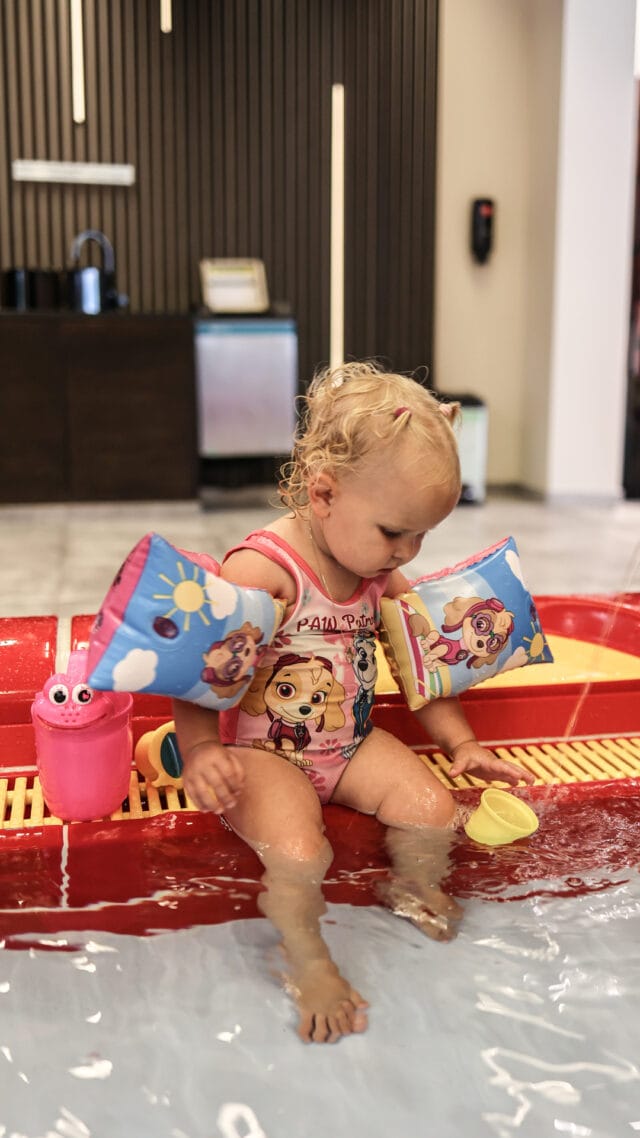 Kleines Kind mit Schwimmhilfen im Wasser spielen.