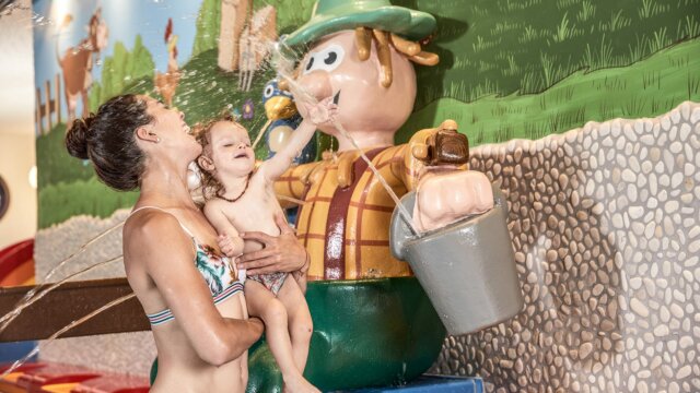 Mutter spielt mit Kind im Spritzwasserbereich.