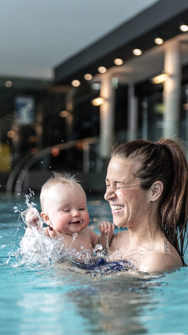 Mutter und Baby im Wasser lachend.