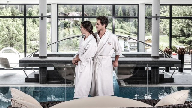 Paar in Bademänteln vor einem Spa-Bereich.