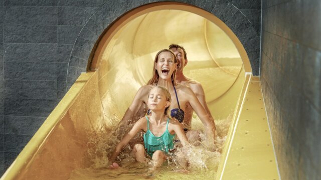 Familie rutscht fröhlich die Wasserrutsche hinunter.