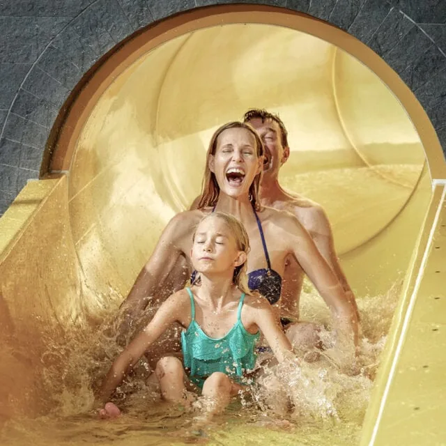 Familie rutscht fröhlich die Wasserrutsche hinunter.