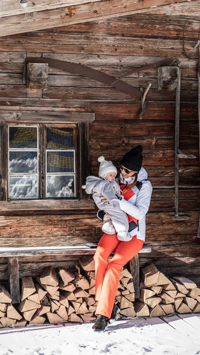 Mutter hält Baby vor einer Holzhütte
