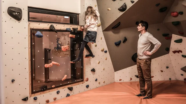 Kind klettert an einer Kletterwand, Erwachsene beobachten.
