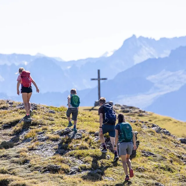 Wanderer auf einem Berg mit kreuzförmigem Gipfel.