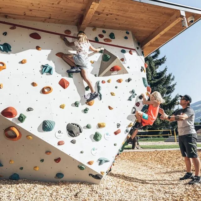 Kinder klettern an einer Kletterwand im Freien.