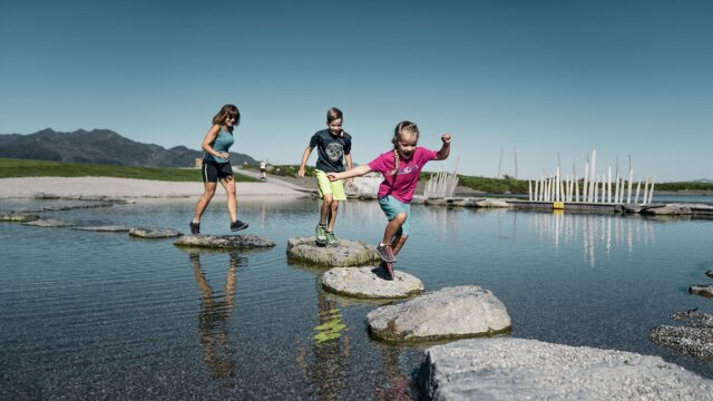 Kinder und Erwachsene springen über Steine im Wasser