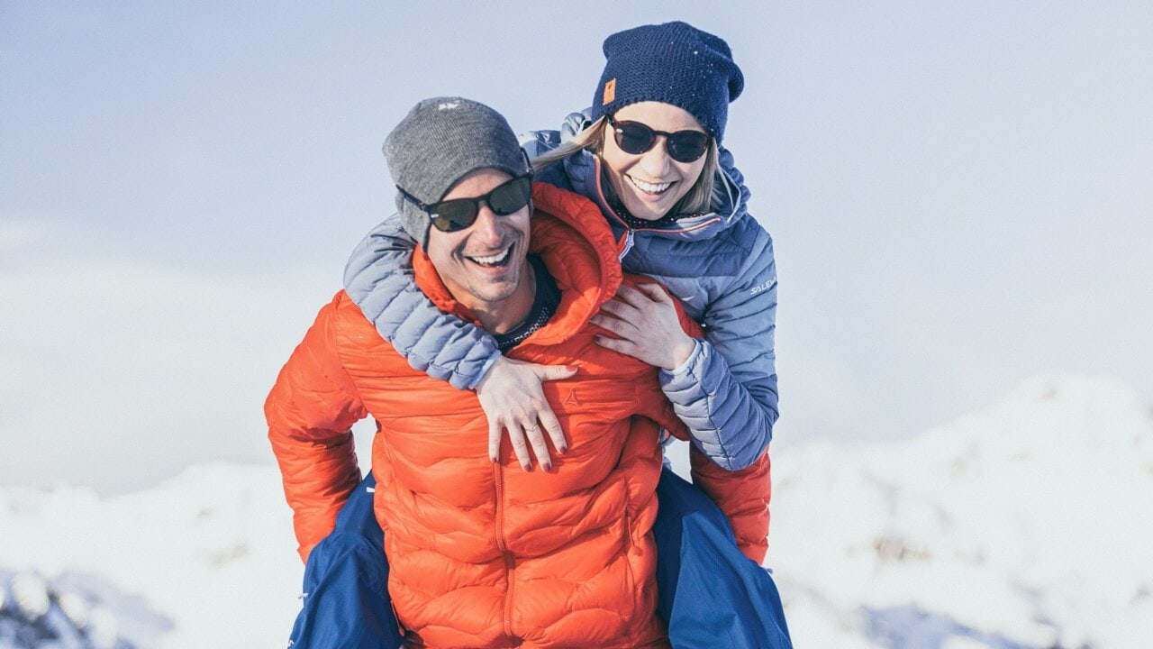 Lächelndes Paar im Schnee mit Outdoor-Bekleidung