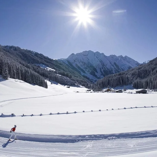 Skifahrer im verschneiten Bergtal mit Sonne