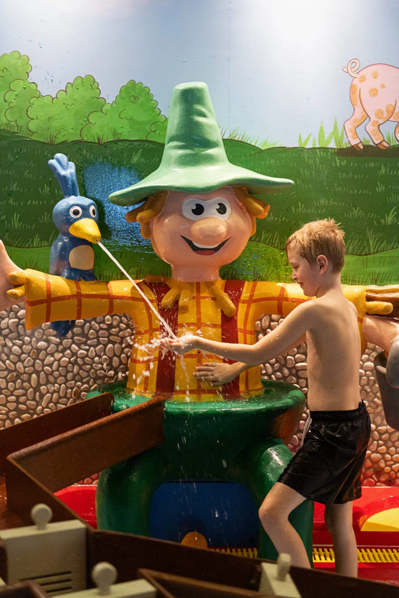 Kind spielt mit Wasser und Figuren im Hintergrund.