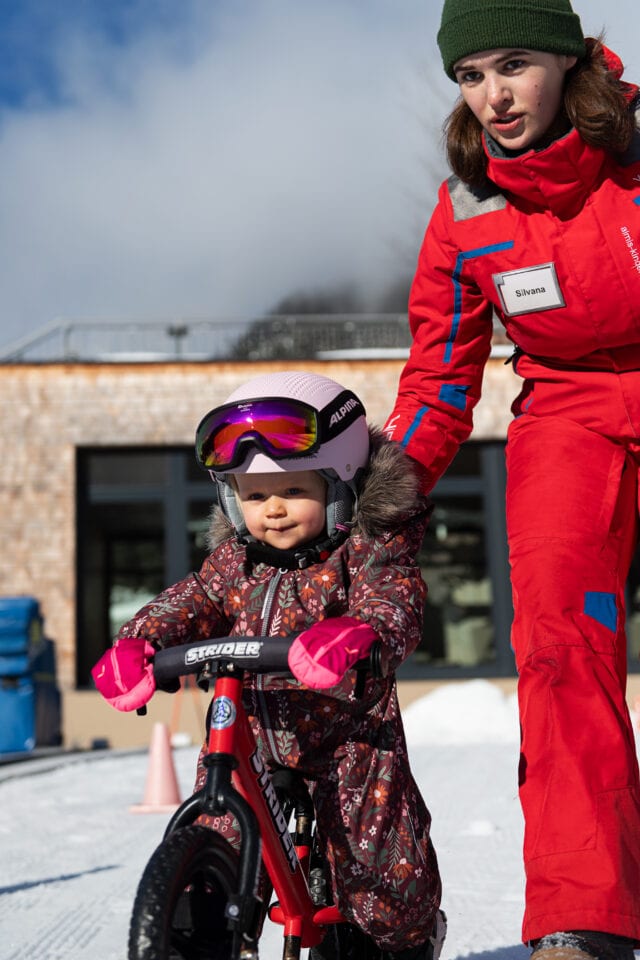 Kind lernt Radfahren mit Anleitung im Schnee.