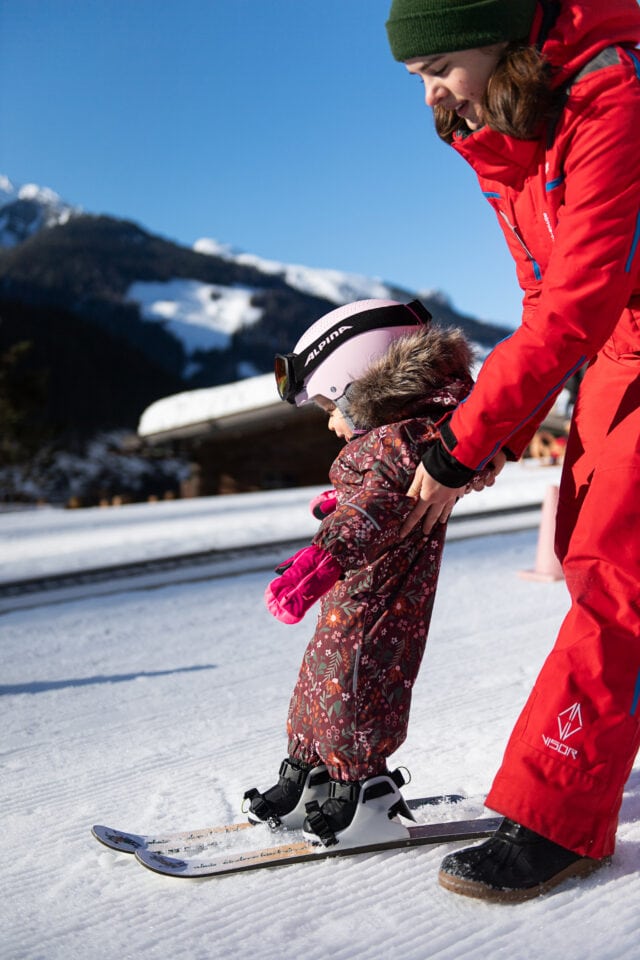 Kind lernt Ski fahren mit Hilfe eines Erwachsenen.