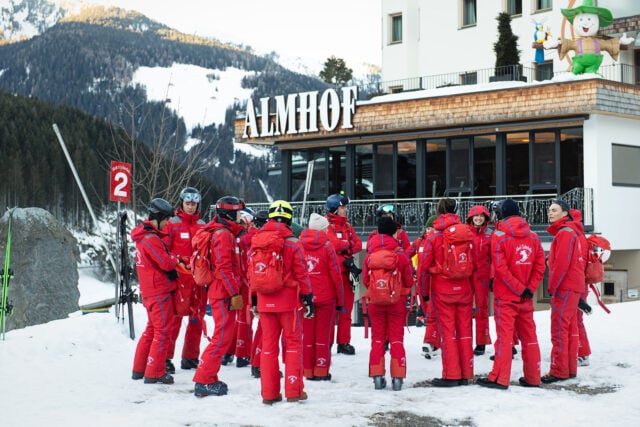 Skifahrer in roten Anzügen vor Hotel Almhof