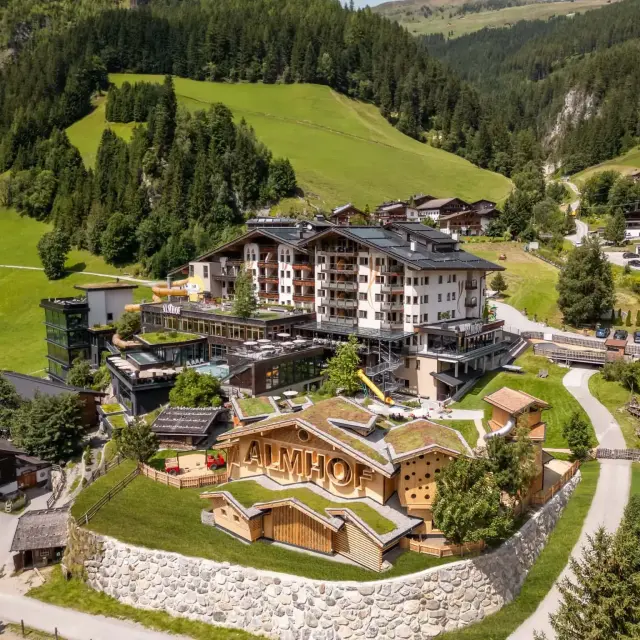 Luftaufnahme des Almhof Hotels in einer grünen Alpenlandschaft.